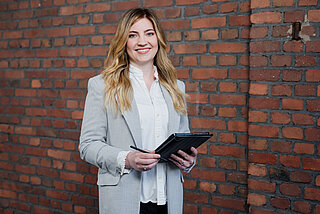 Frau mit einem Tablet in der Hand steht vor einer verklinkerten Mauer